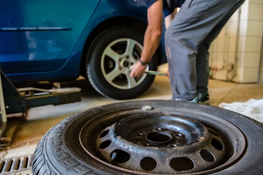 A close up of a spare tyre and a mechanic replacing tyres of a blue car in the background