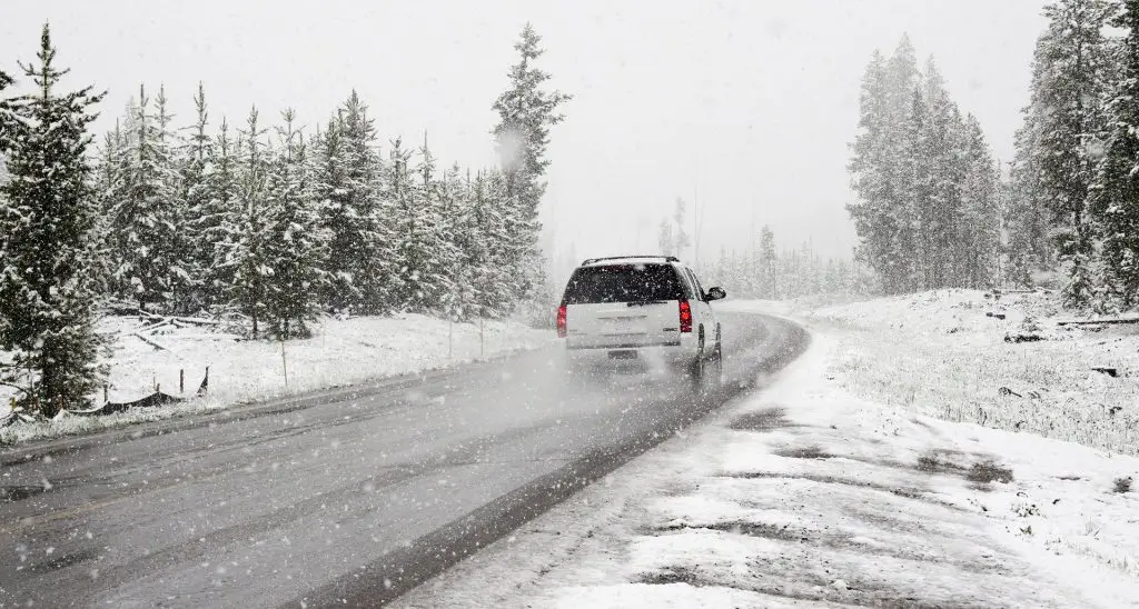 Tail light of white SUV approaching a curve under a snowfall