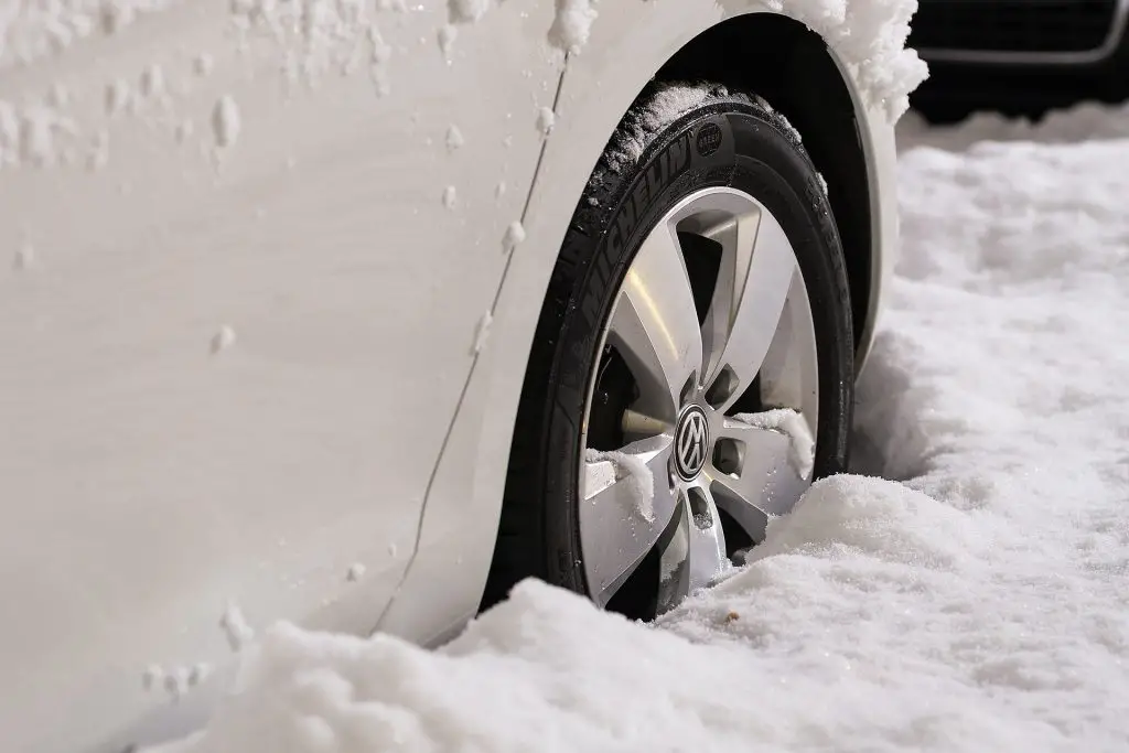 Right front tyre of a white car party buried in snow.