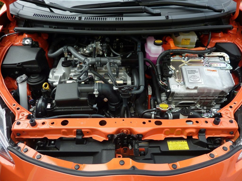 Inside the bonnet of an orange vehicle showing the battery, engine and other parts